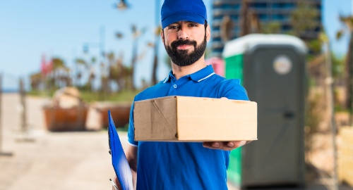 Delivery man dressed in blue holding a parcel in one hand and a folder in the other, facilitating prescription home delivery. Delivery man dressed in blue holding a parcel in one hand and a folder in the other, facilitating prescription home delivery.